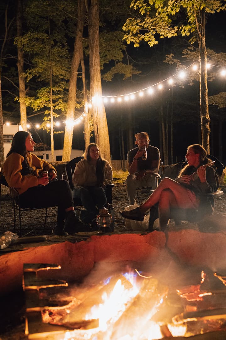 Friends gathered around a campfire with string lights
